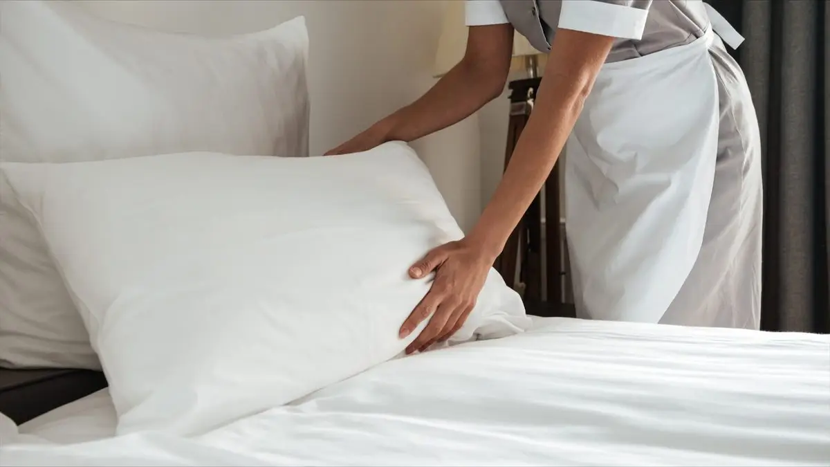 Hotel maid making bed with white sheets